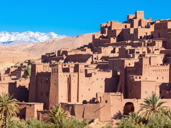 a desert town with palm trees and mountains in the background with Aït Benhaddou in the background
