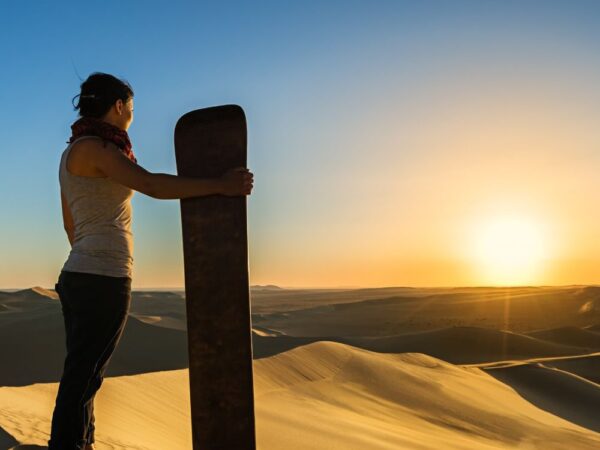 a woman standing in the sand with a sandboard