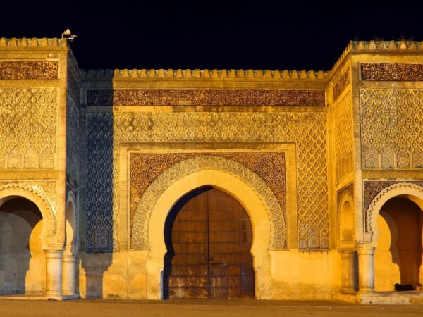 a large ornate building with arched doorways with Meknes in the background